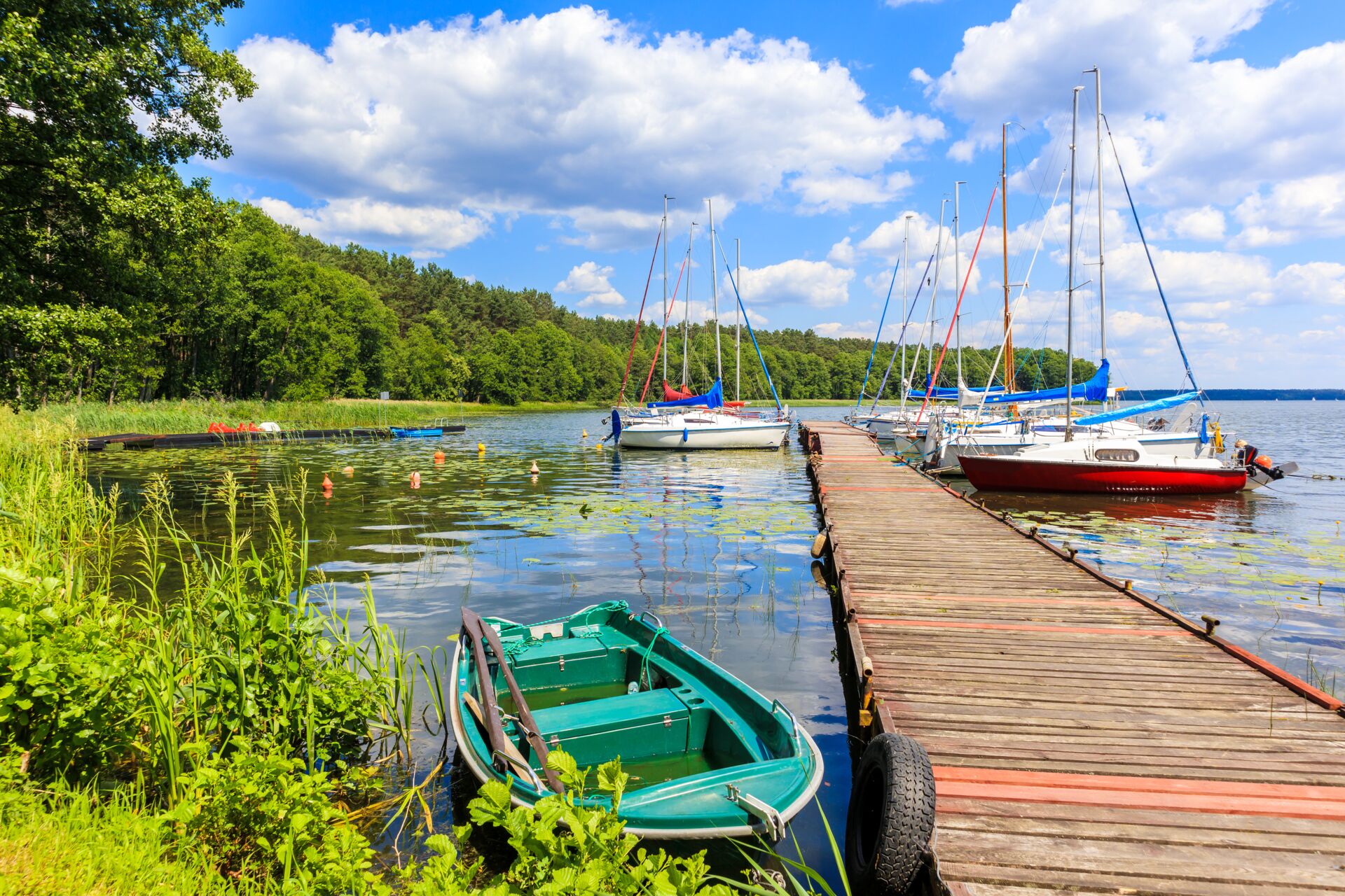 Segelboote und ein Ruderboot an einem Steg in Masuren, symbolisieren die vielfältigen Wassersportmöglichkeiten