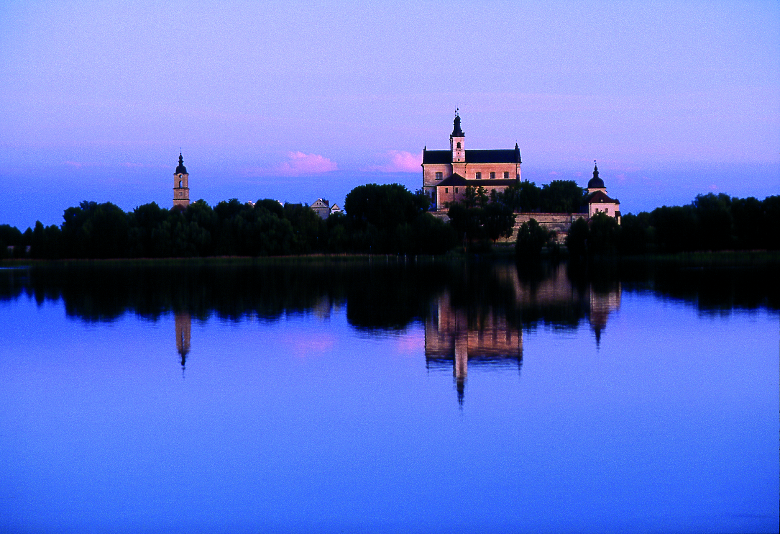 Ein historisches Gebäude, möglicherweise ein Kloster oder eine Kirche, am Ufer eines Sees in Masuren